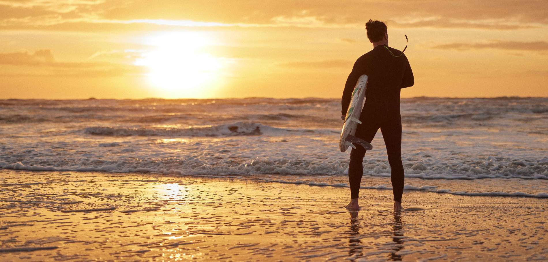 Một vận động viên lướt sóng mặc bộ đồ lặn đang phân tích, đánh giá các con sóng vào khoảnh khắc mặt trời mọc
